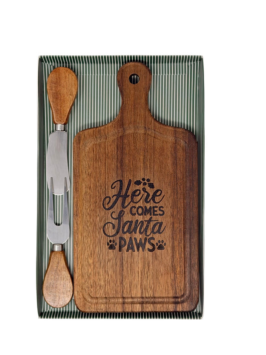 Hand-burned Here Comes Santa Paws cheeseboard with wood-handled cheese knife and fork in a green striped gift box